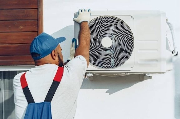 Repairman in uniform installing the outside unit of air conditioner